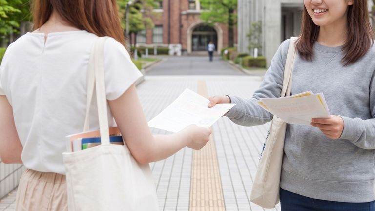 大学構内で学生にチラシを手渡ししている学内サンプリングの実施イメージ