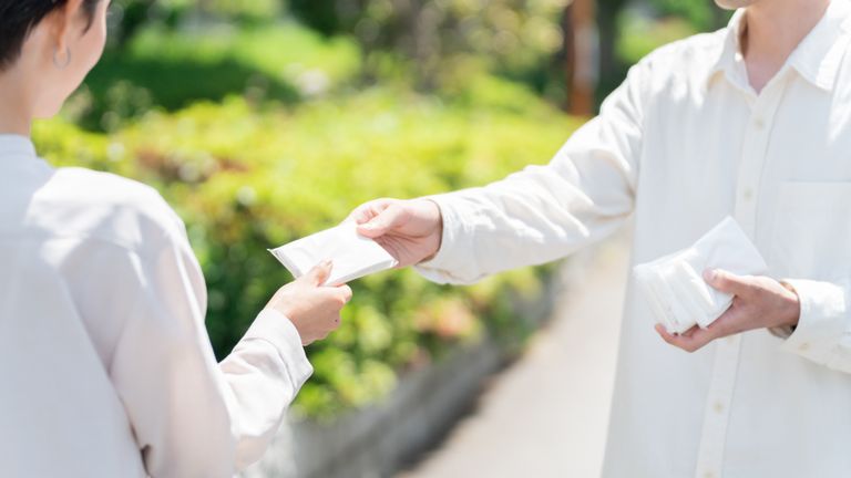 大学の校門前で学生にポケットティッシュを手渡ししている校門前サンプリングの実施イメージ